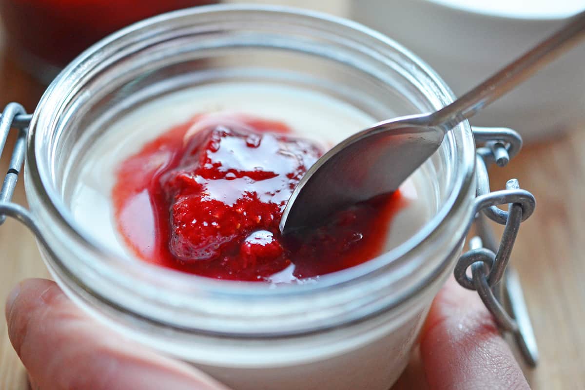 A small spoon is scooping into a jar of strawberry Panna Cotta.