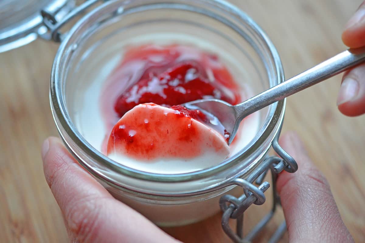 Scooping out a spoonful of strawberry Panna Cotta from a glass jar.