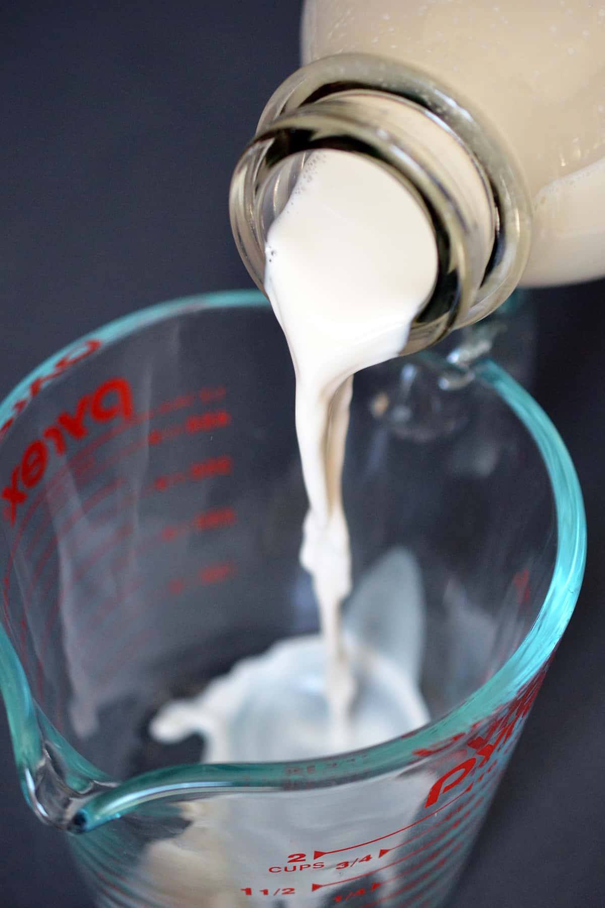 Pouring almond milk into a glass measuring cup.