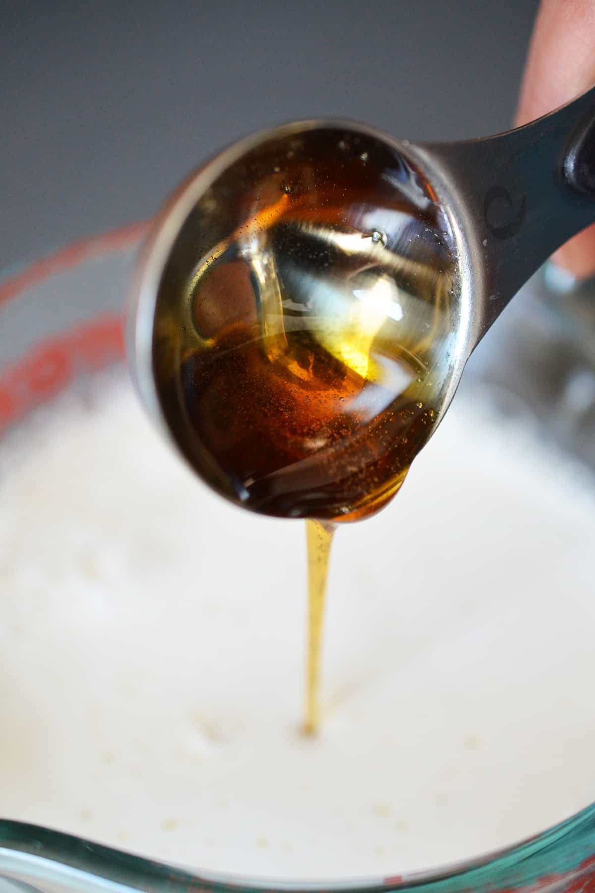 Pouring maple syrup into a measuring cup filled with homemade almond milk.