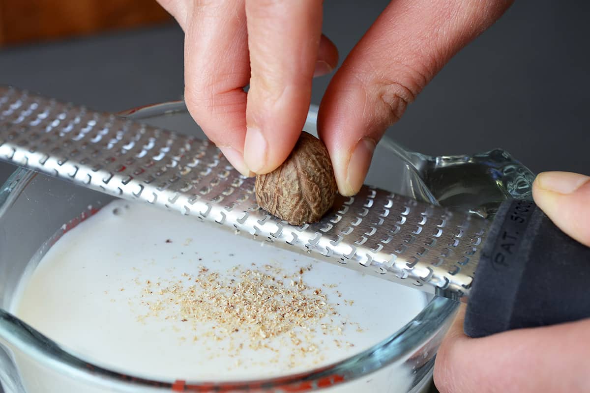 Grating nutmeg with a microplane rasp grater into a measuring cup filled with sweetened almond milk.