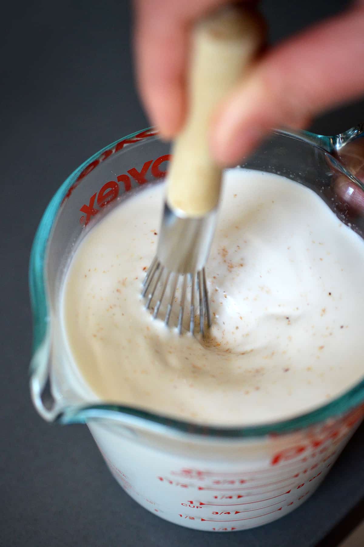Whisking together the ingredients to make homemade dairy-free Panna Cotta with almond milk in a glass measuring cup.