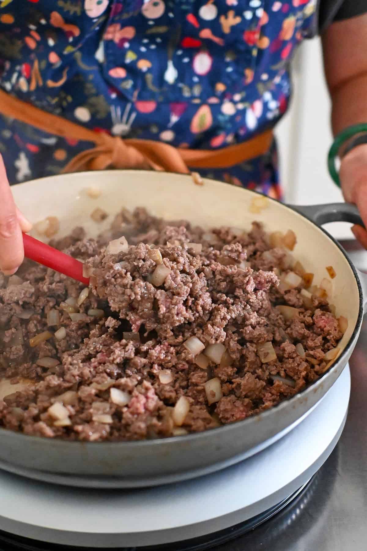 A closeup of ground beef and onions in a large gray skillet cooked until the beef is no longer pink.