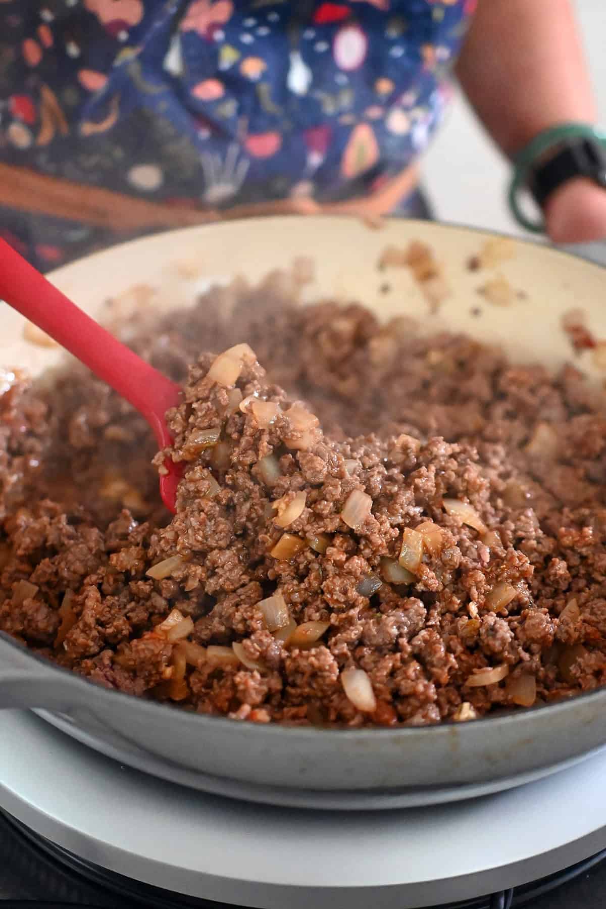A closeup of the seasoned ground beef and onions before the vegetables and sauce are added to the skillet.