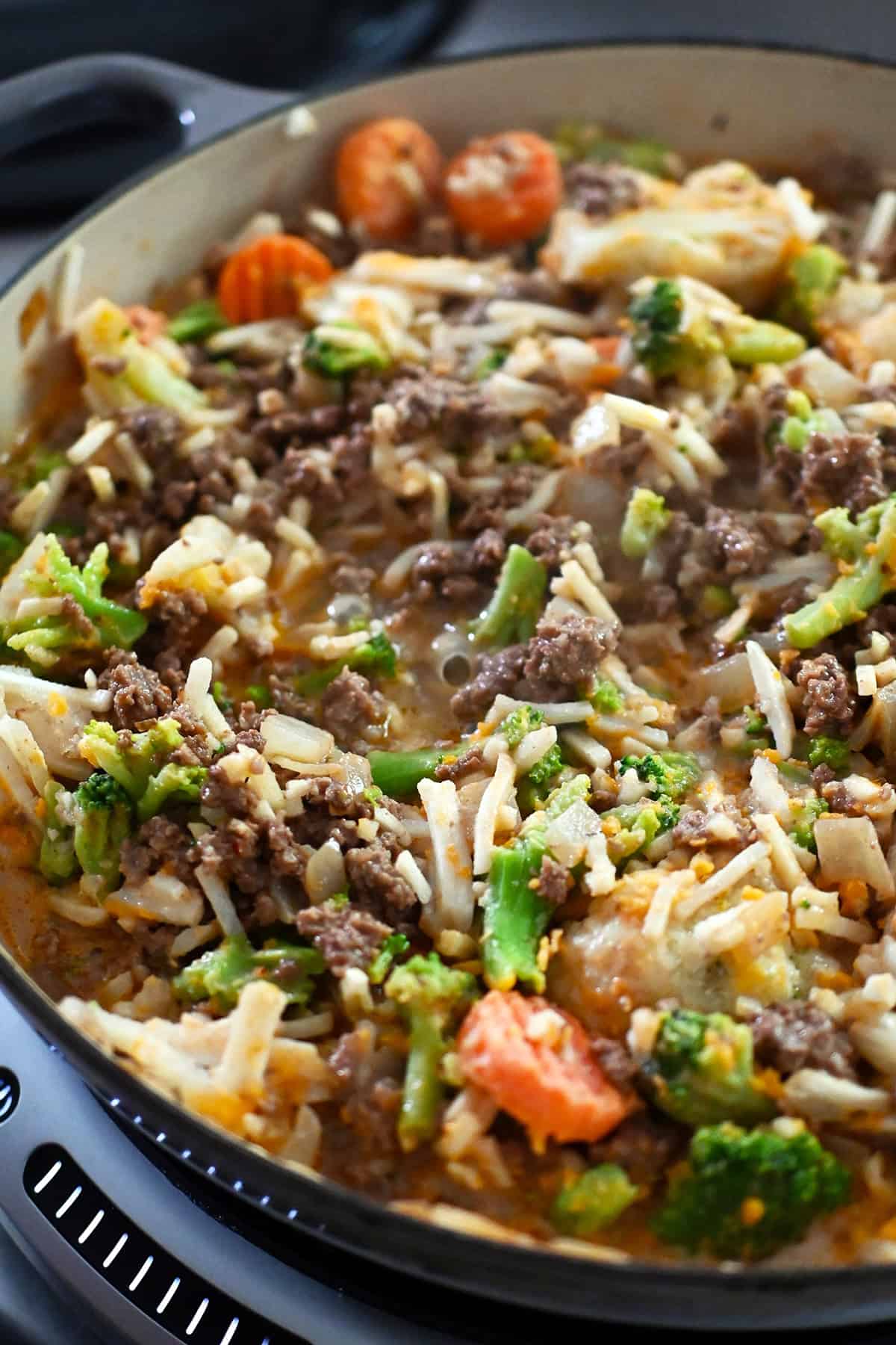 A closeup of the combined veggies, ground beef, and shredded potatoes in a large gray skillet before the lid is put on and the skillet is brought to a simmer.