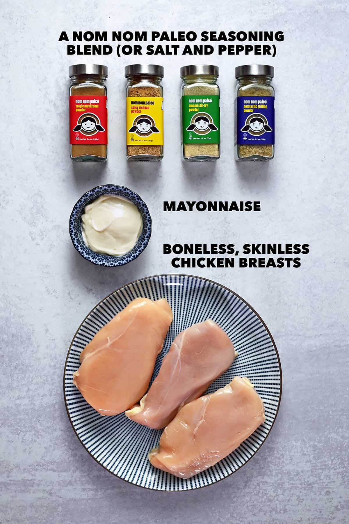 An overhead shot of the raw ingredients to make foolproof chicken breasts: boneless and skinless chicken breasts on a plate, Nom Nom Paleo seasoning blends, and some mayonnaise.