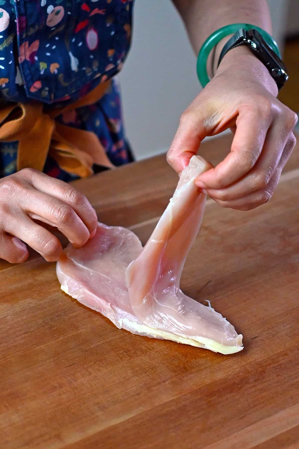 A hand is separating a raw boneless skinless chicken breast that has been cut in half horizontally.