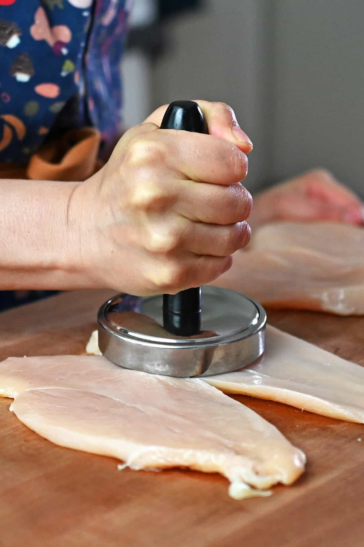 Pounding thinly cut boneless skinless chicken thighs with a meat pounder.