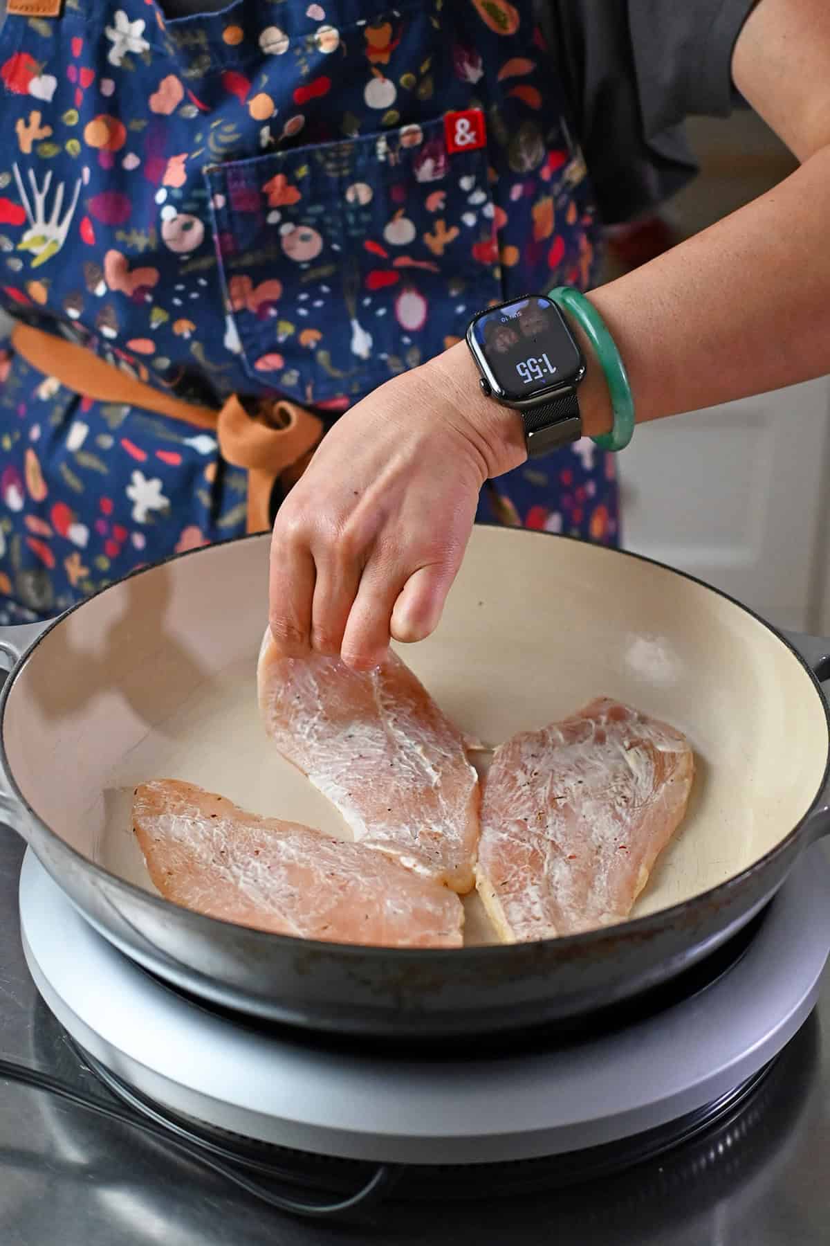 Adding a boneless skinless chicken breast coated with a thin layer of mayonnaise and seasoning into a skillet.