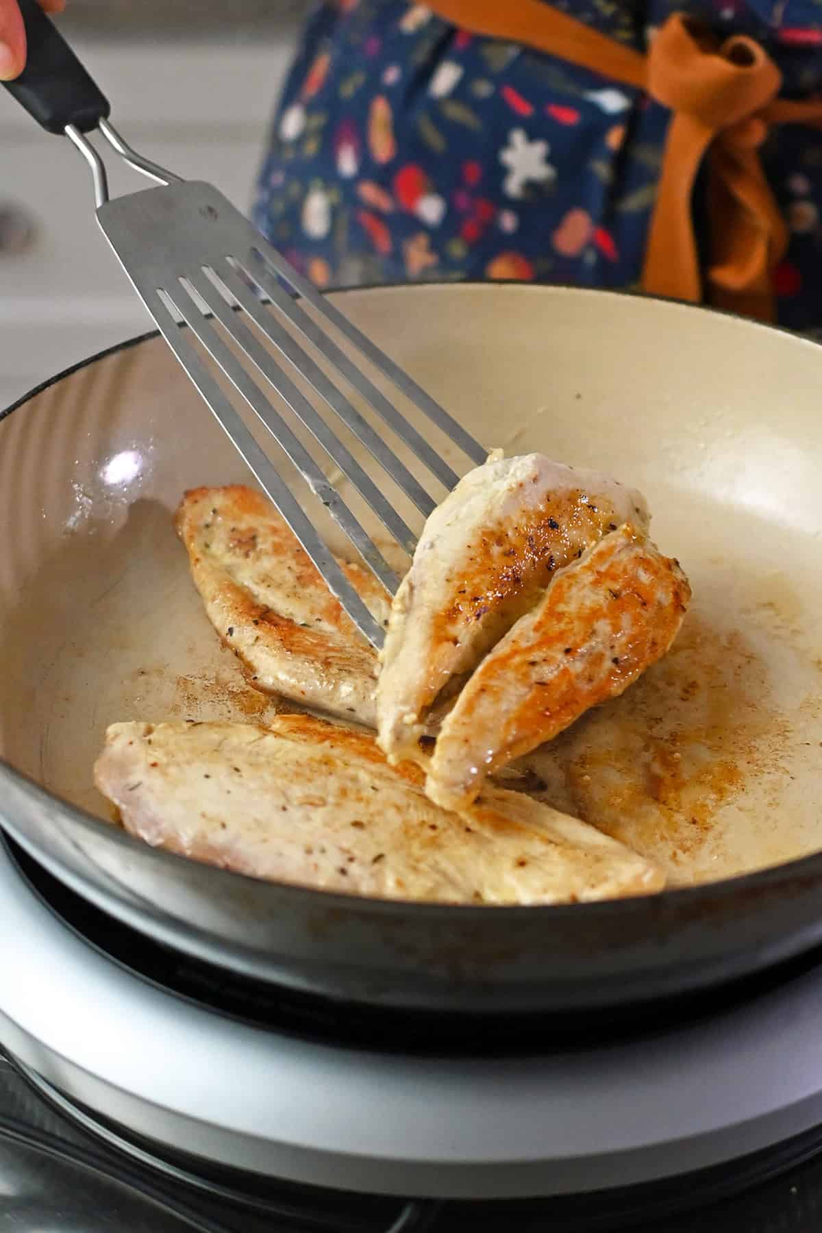 Flipping a boneless skinless chicken breast in a skillet with a fish spatula.